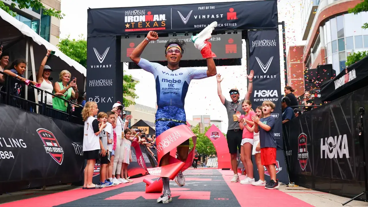 A triumphant athlete breaks the tape at the Memorial Hermann Ironman Texas, celebrating a victory in this demanding team triathlon event.