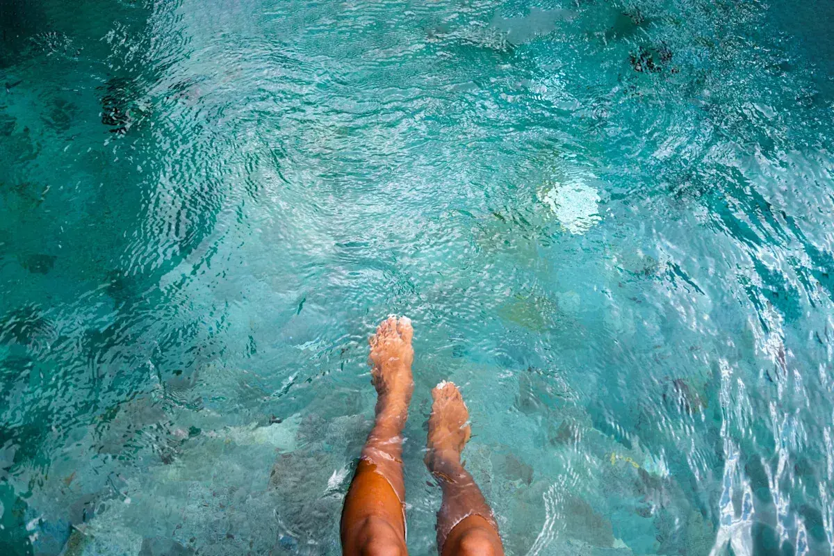 Feet submerged in clear turquoise water, with small fish swimming around. A person wonders if they can swim with a yeast infection.