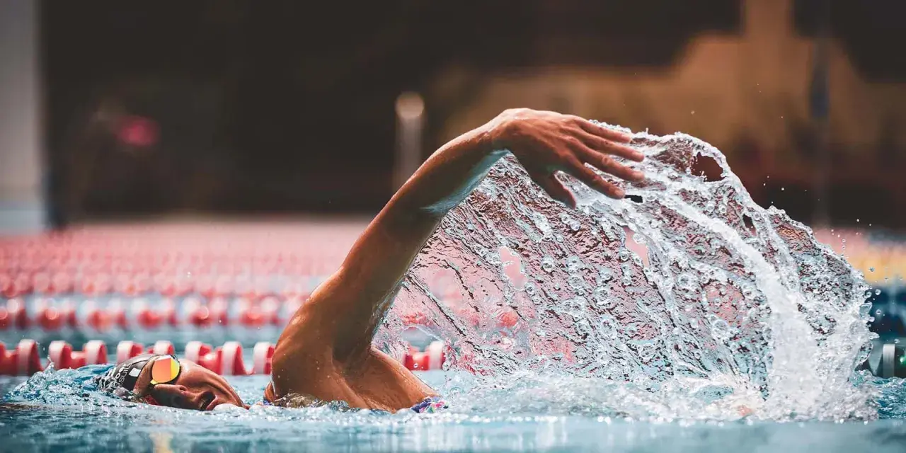 A swimmer's arm slices through the water, creating a dramatic splash during a powerful stroke. The focus is on the dynamic movement as they swim.