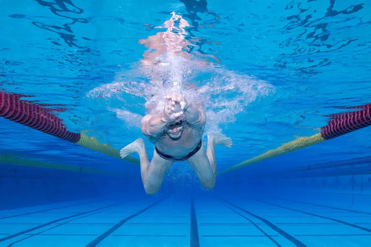Underwater view of a man performing the breast stroke in a swimming pool, with lane lines and buoys visible.