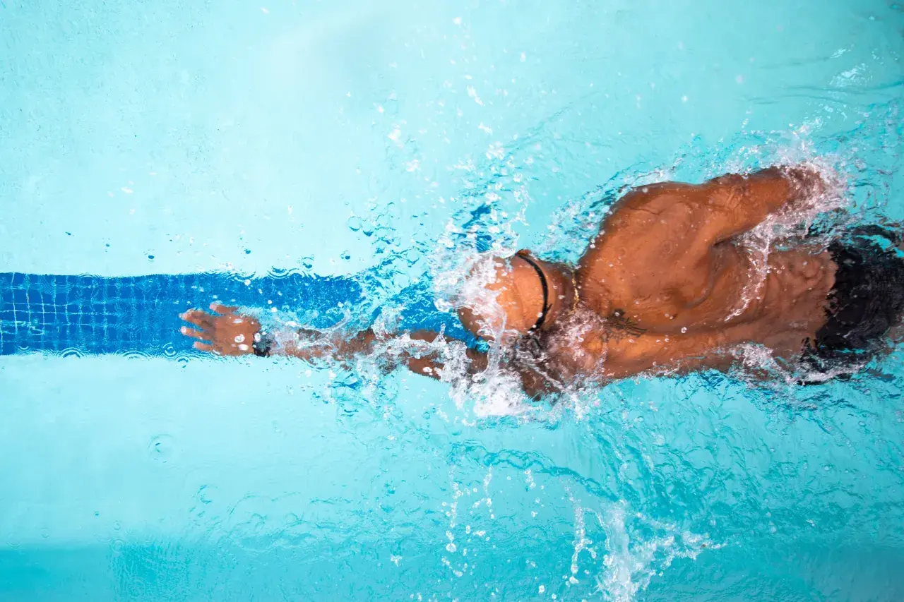 A swimmer powers through the water, creating splashes. This image inspires questions about how long to swim for exercise.