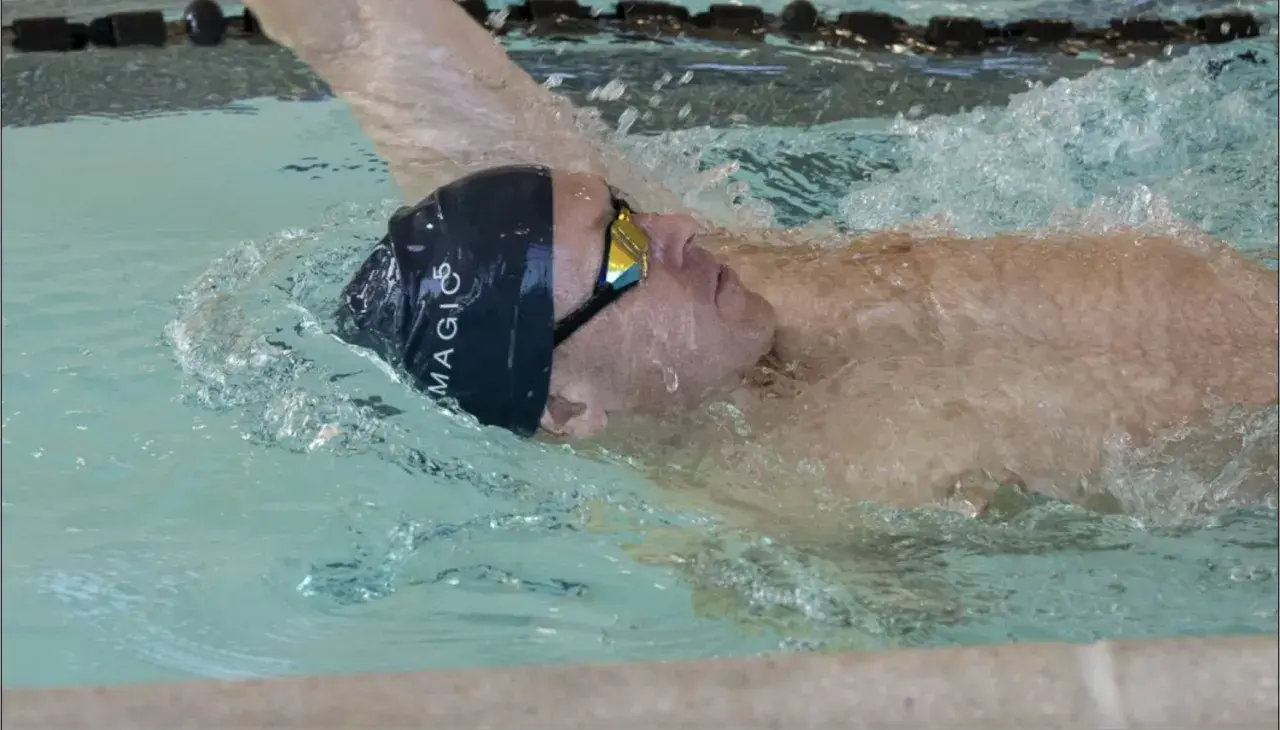 Swimmer executing a backstroke flip turn, water splashing around their head and goggles.