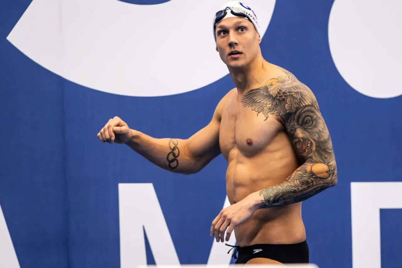 A muscular swimmer with extensive tattoos, including Olympic rings, prepares for a race, showcasing his dedication to swim conditioning.