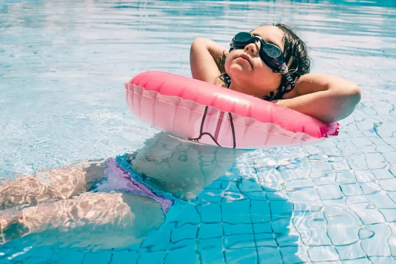A child relaxes in a pool with a pink float, enjoying a moment of peace after swim lessons for 1 year old.