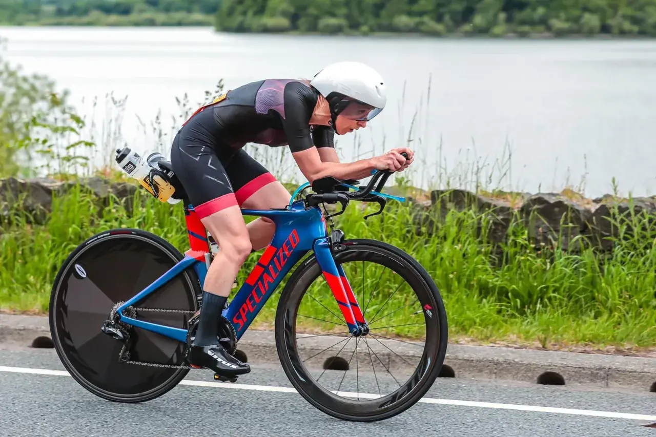 Athlete in a road triathlon, focused and aerodynamic on a blue and red Specialized bike, with a lake in the background.