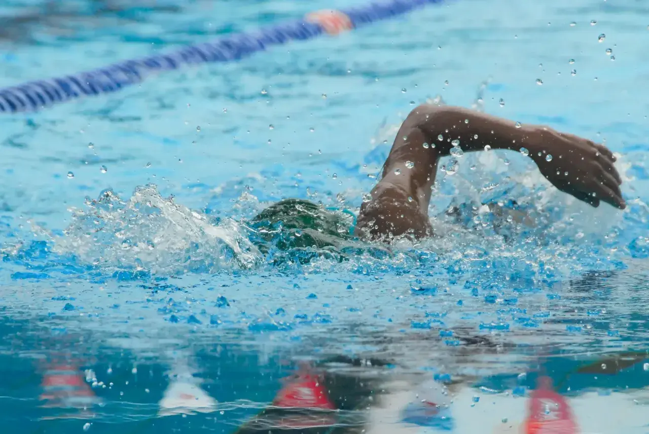 A swimmer powers through the water, mid-stroke, during an intense 1 hour swim workout. Splashes and bubbles fly.