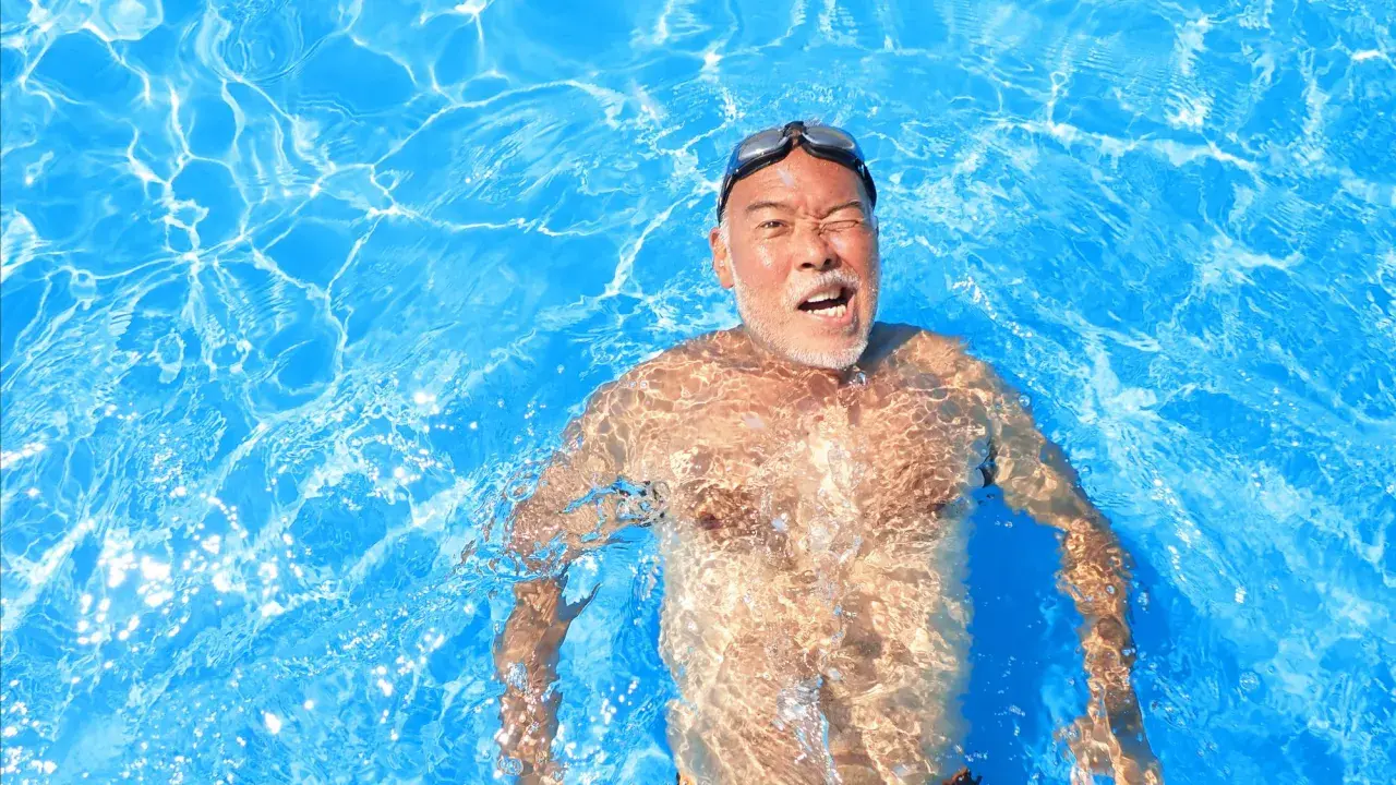 Man in pool, goggles on, with a surprised expression, experiencing immersion diuresis.