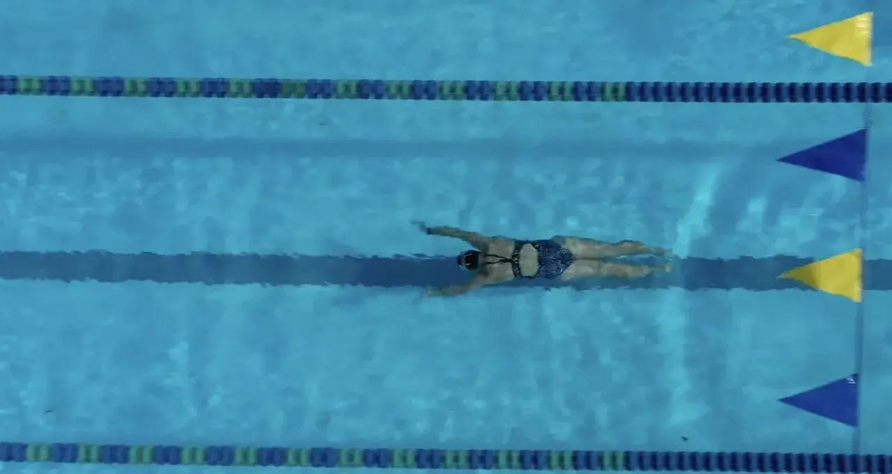A swimmer glides through the water, executing a powerful breaststroke. The blue pool is marked with lane lines and colorful flags.