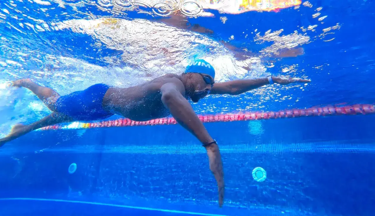 Swimmer in blue cap and goggles glides through the water, a powerful stroke that can help you increase your VO2 max.