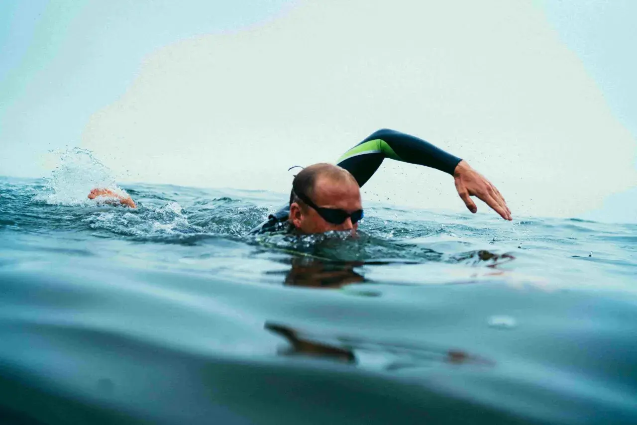 Swimmer in goggles and wetsuit performs swim drills, with one arm extended and splashing water.