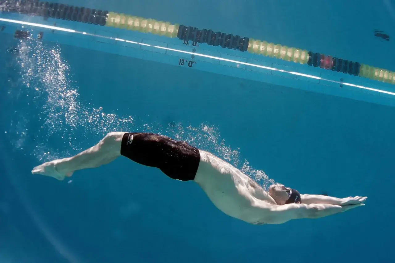 Underwater view of a swimmer performing a powerful kick, showcasing effective leg workouts for swimmers. Bubbles trail behind as they glide through the blue water.