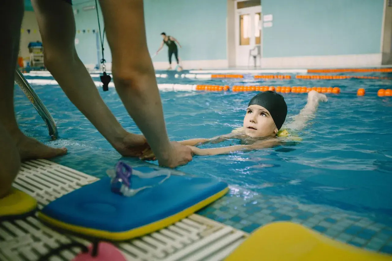 A child learns to swim with an instructor's help, experiencing the benefits of water safety and physical activity.