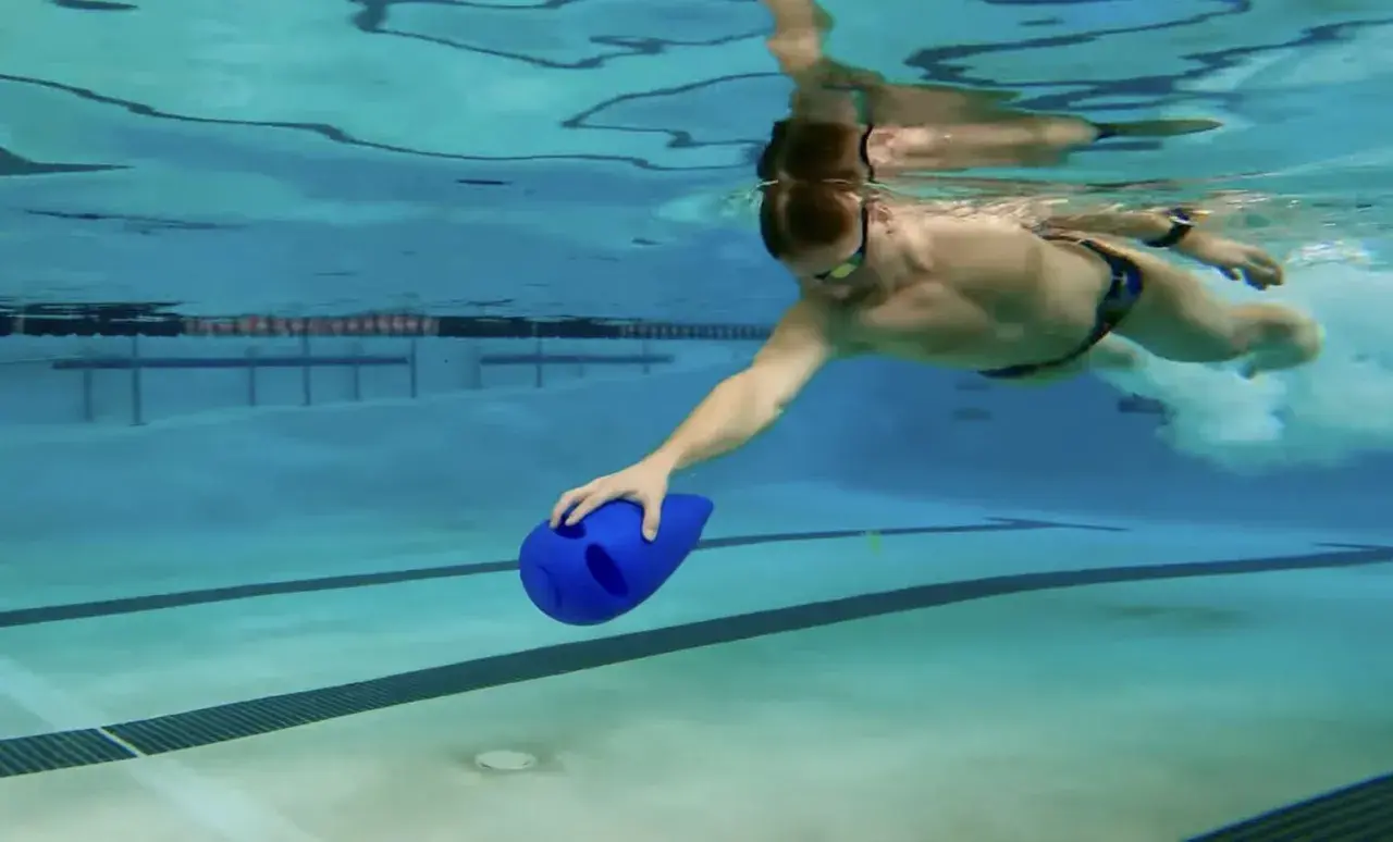 Man swimming underwater with a blue kickboard, practicing his kickboard swim technique.
