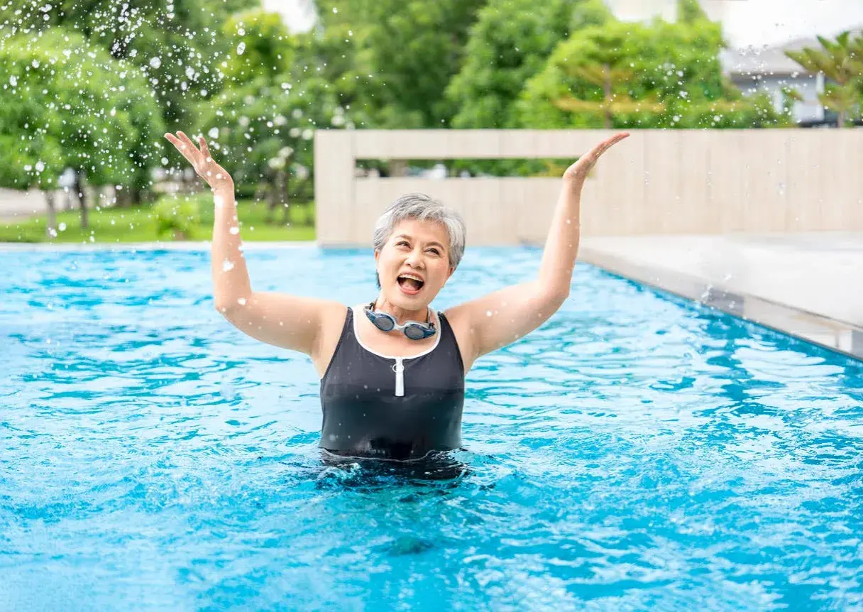 Joyful senior woman splashing water in a pool, enjoying her beginner swim workout.