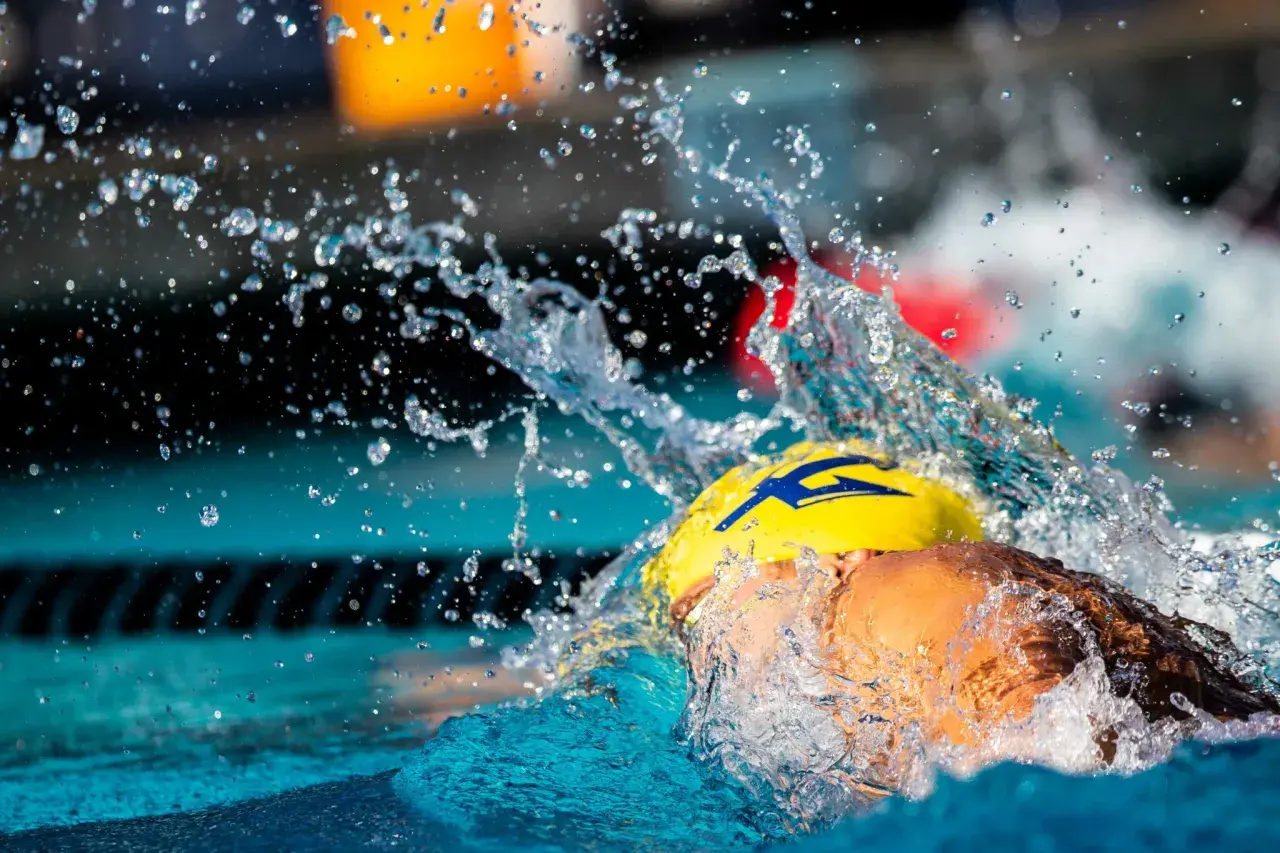 A swimmer in a yellow cap with a blue lightning bolt, mid-stroke, creating a dramatic splash. This captures the intense swolf meaning of speed and power.