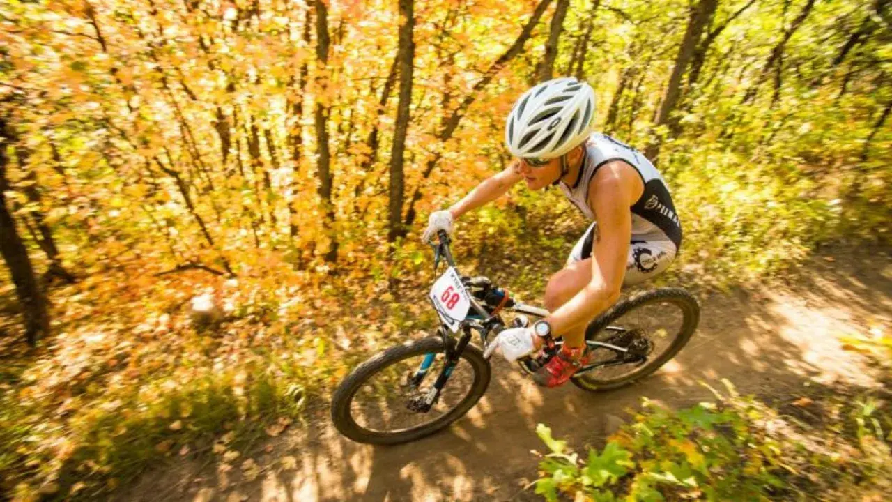 Athlete races through an autumn forest during an off road triathlon, navigating a dirt path with colorful foliage.
