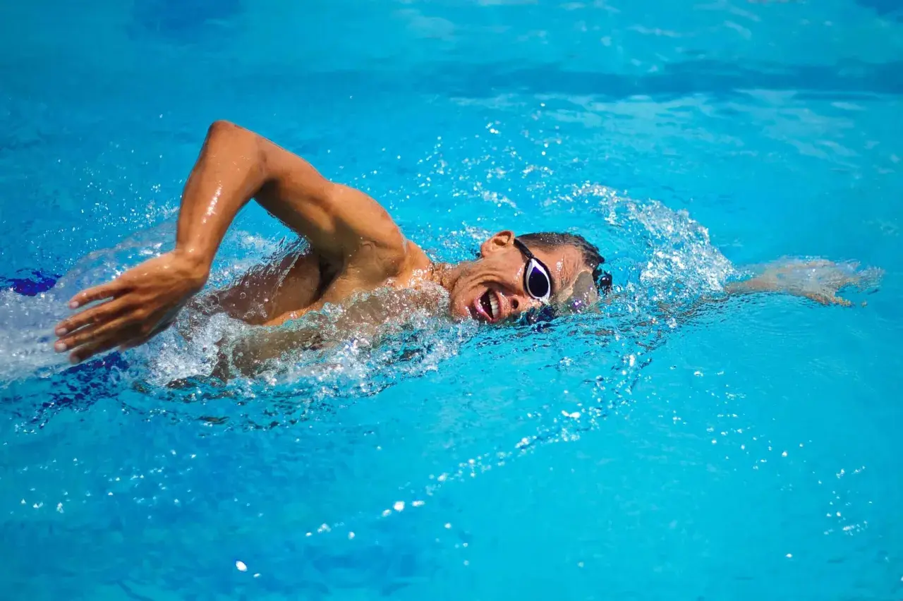 Swimmer with goggles in bright blue water, performing bilateral breathing during a freestyle stroke.