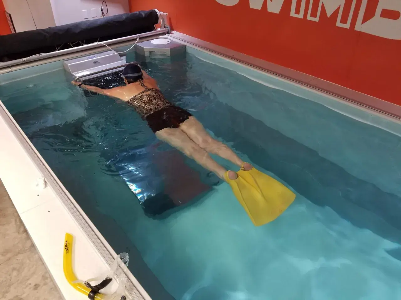 Woman with yellow fins practicing her leg kicking in a swim spa.