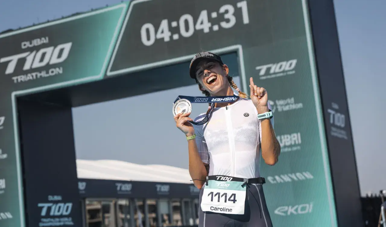 Caroline celebrates her finish at the Dubai T100 Triathlon, medal in hand, under the finish arch.