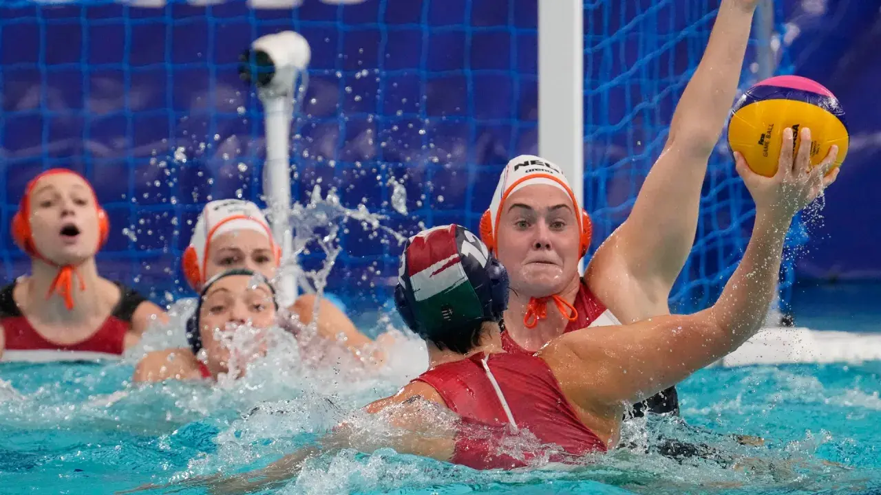 Intense water polo action, with players battling for the ball. The struggle suggests potential water polo fouls as they jostle for position near the goal.