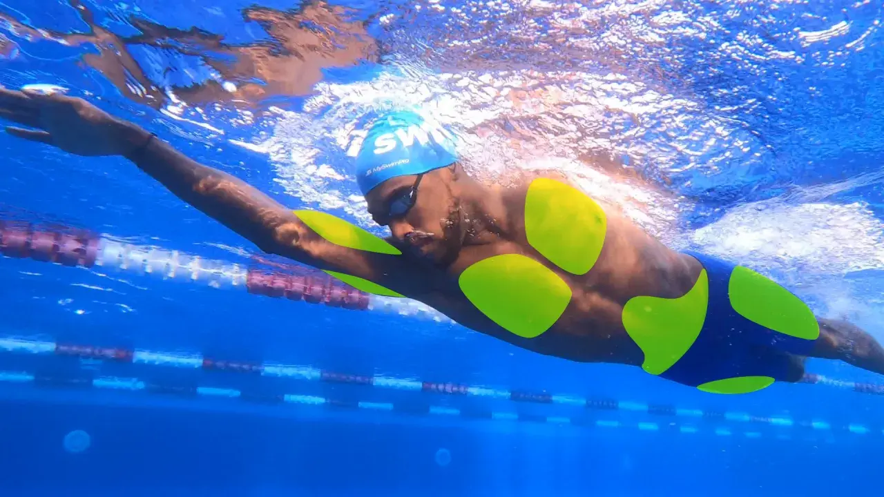 A swimmer's body, with neon green highlights on their torso and arms, glides through a blue pool.
