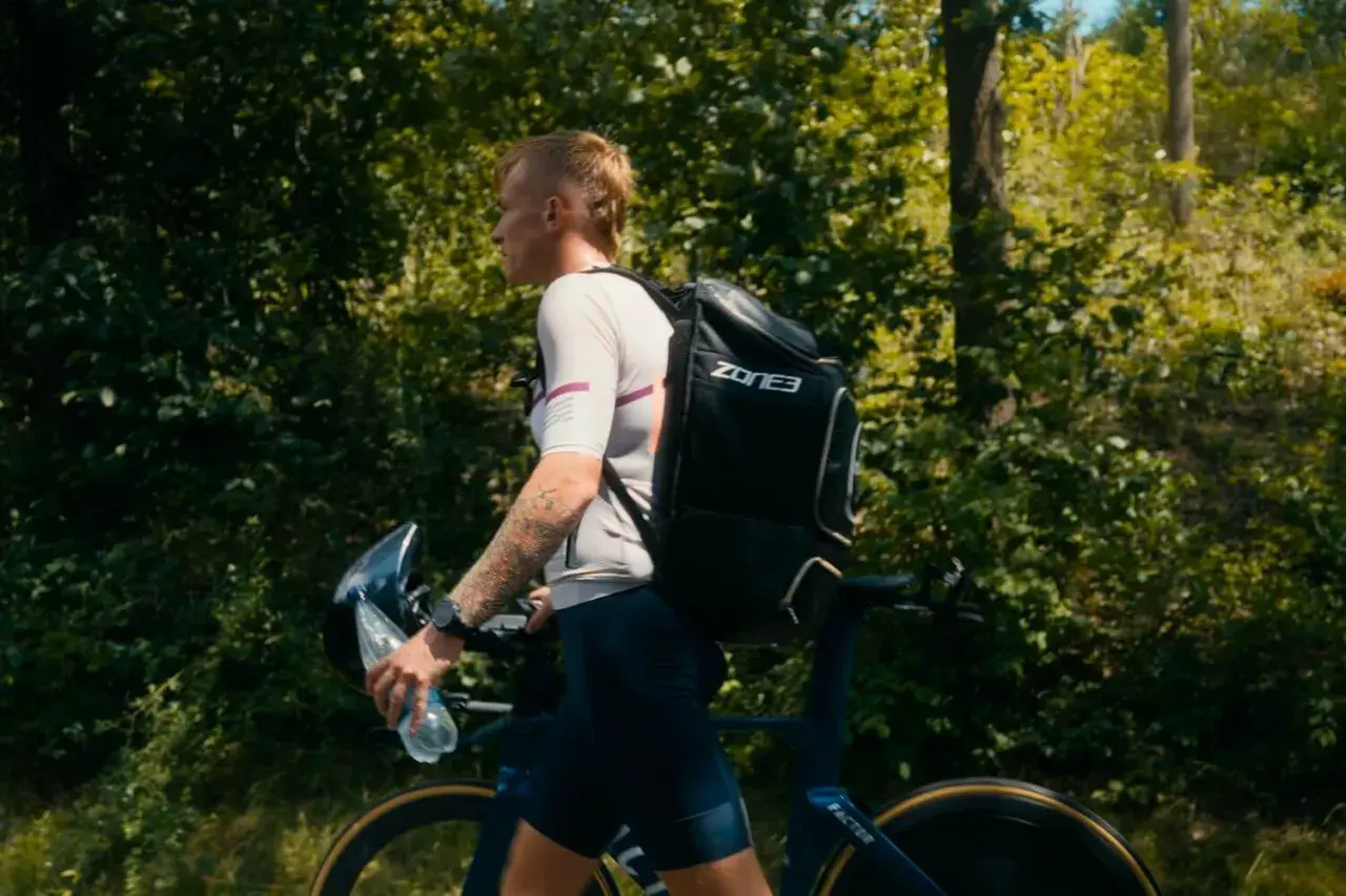 Athlete walks with bike and gear, preparing for the next stage in triathlon transition areas.