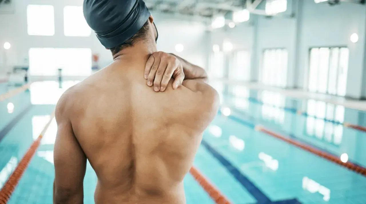 Swimmer holding shoulder in pain, questioning if you can swim with a torn rotator cuff.