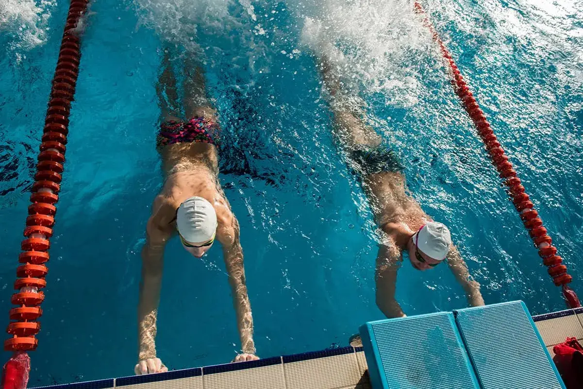 Two swimmers practice their flutter kicks, pushing off the wall in a race.