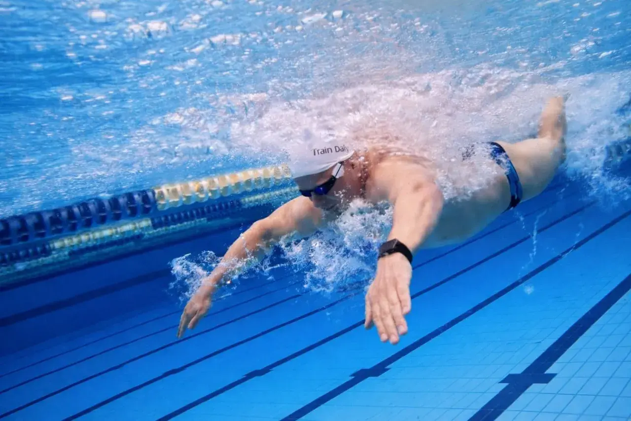 Swimmer executing a powerful butterfly stroke underwater, creating a splash as they propel through the blue pool lanes.