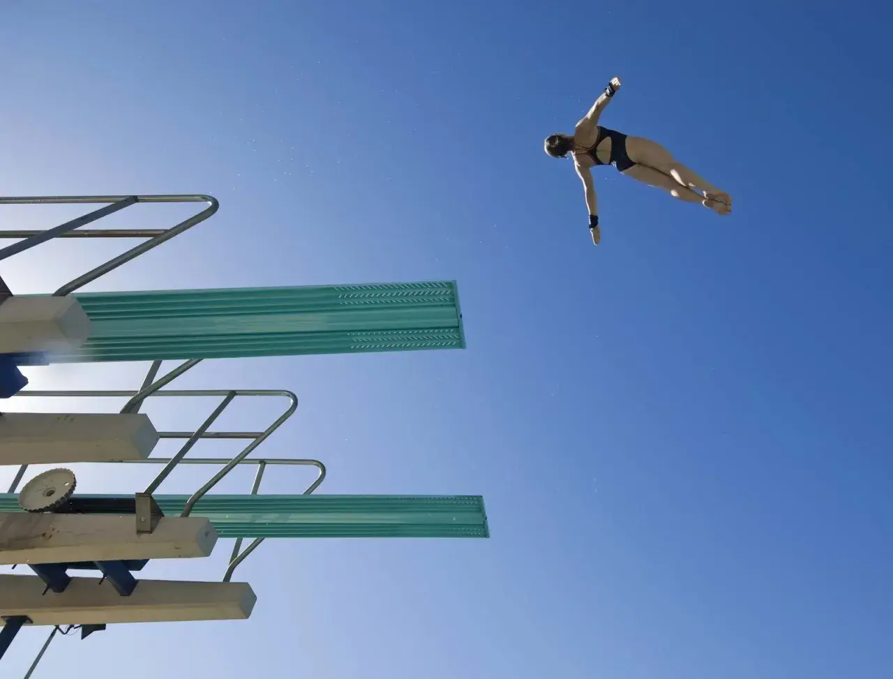 A diver in mid-air, performing a competitive dive against a clear blue sky.