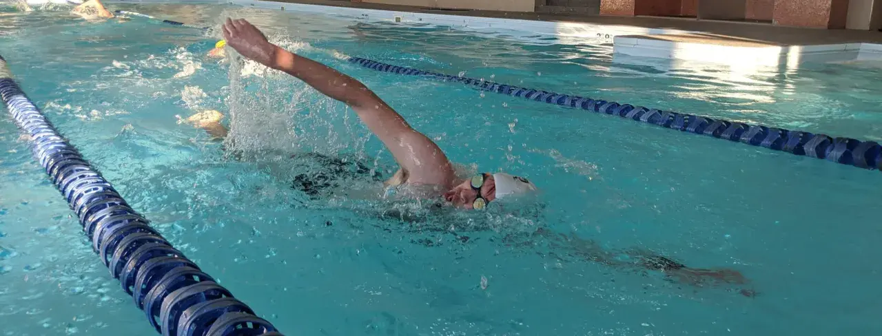 Swimmer pushing hard in a pool, arms extended, water splashing. This intense effort is part of a challenging vo2 max workout.