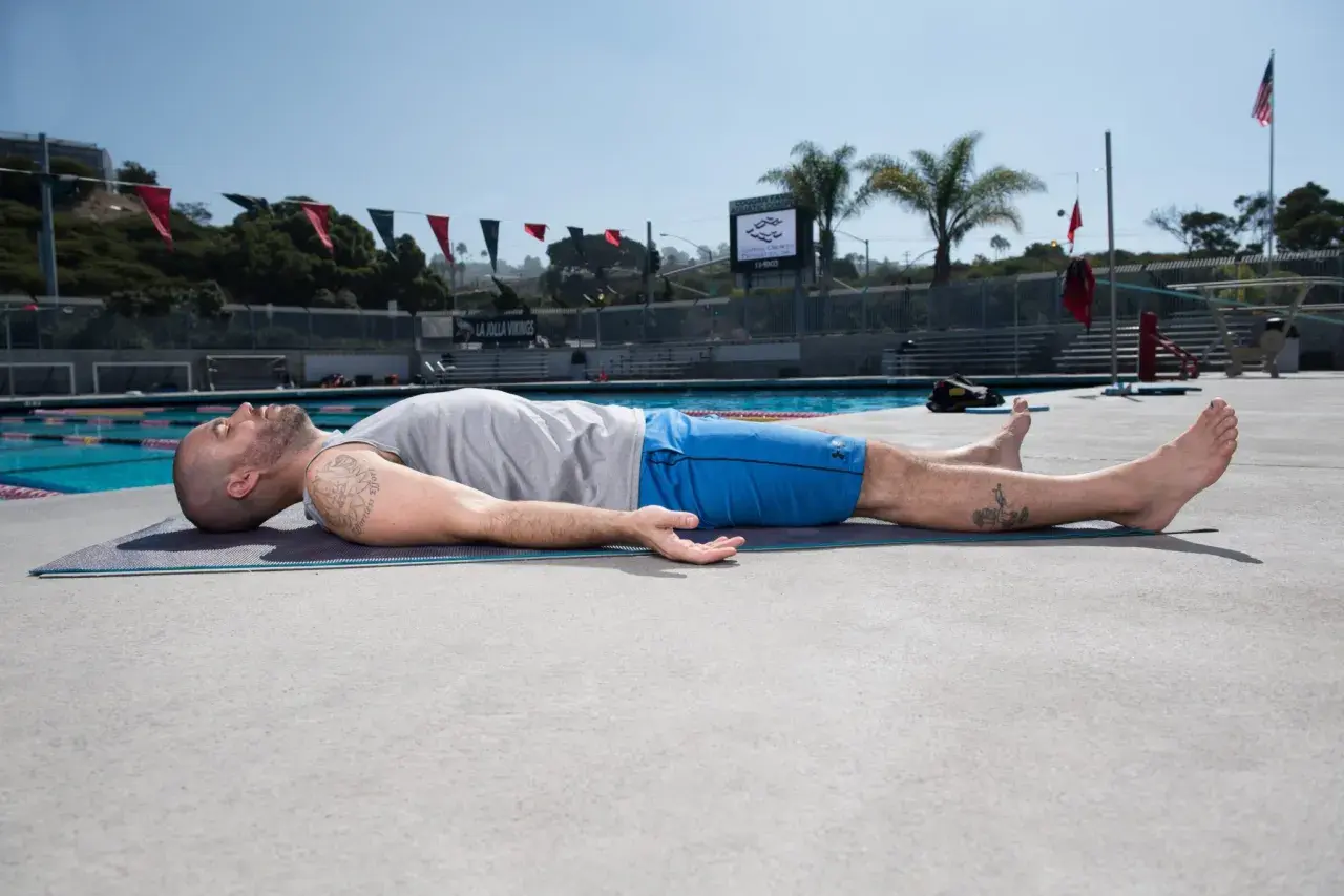 Man practicing yoga for swimmers, lying on a mat by the pool, enjoying a moment of relaxation and recovery.