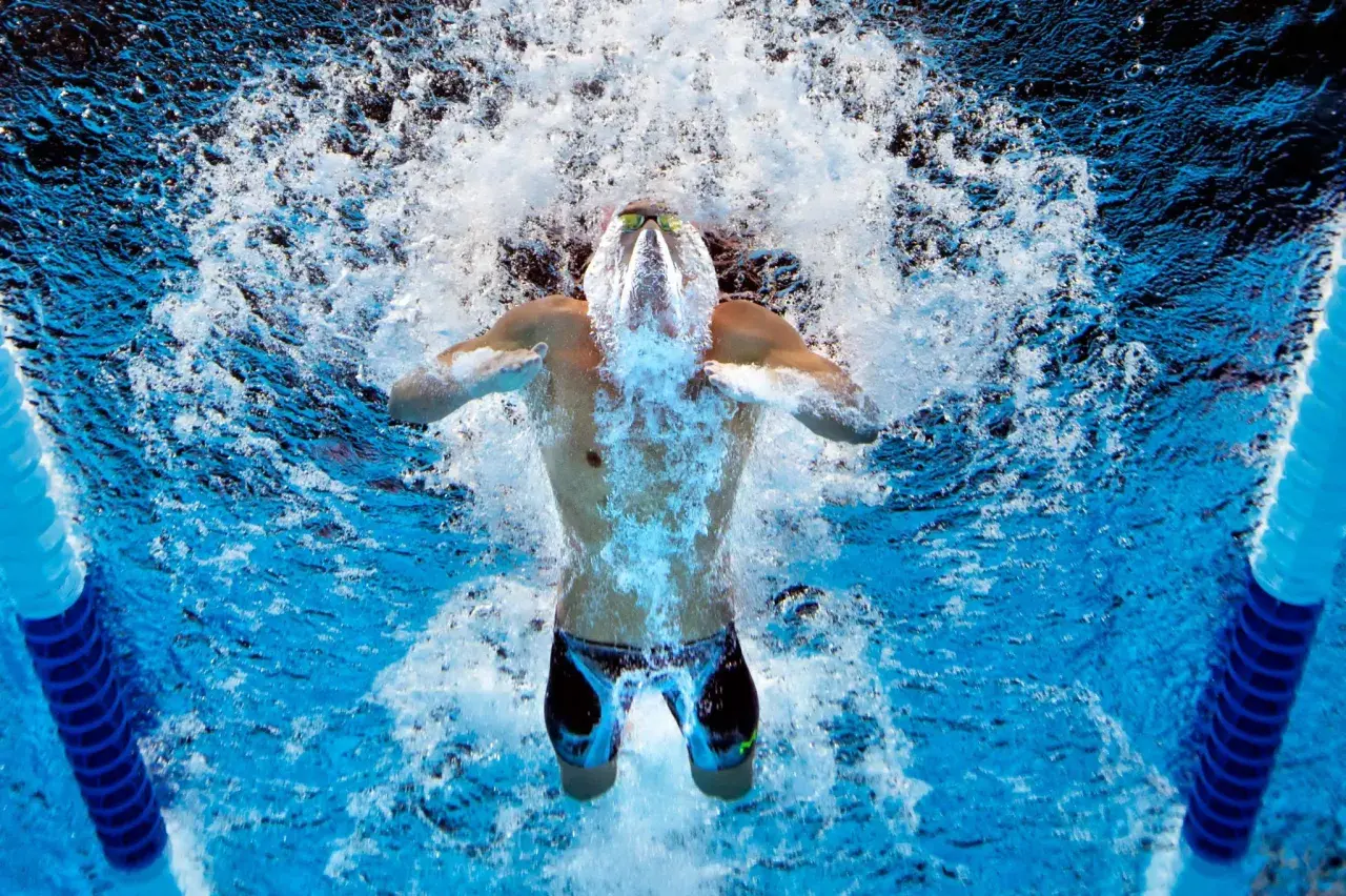 Swimmer powering through intense swim practice sets, creating a splash as they break the water's surface.