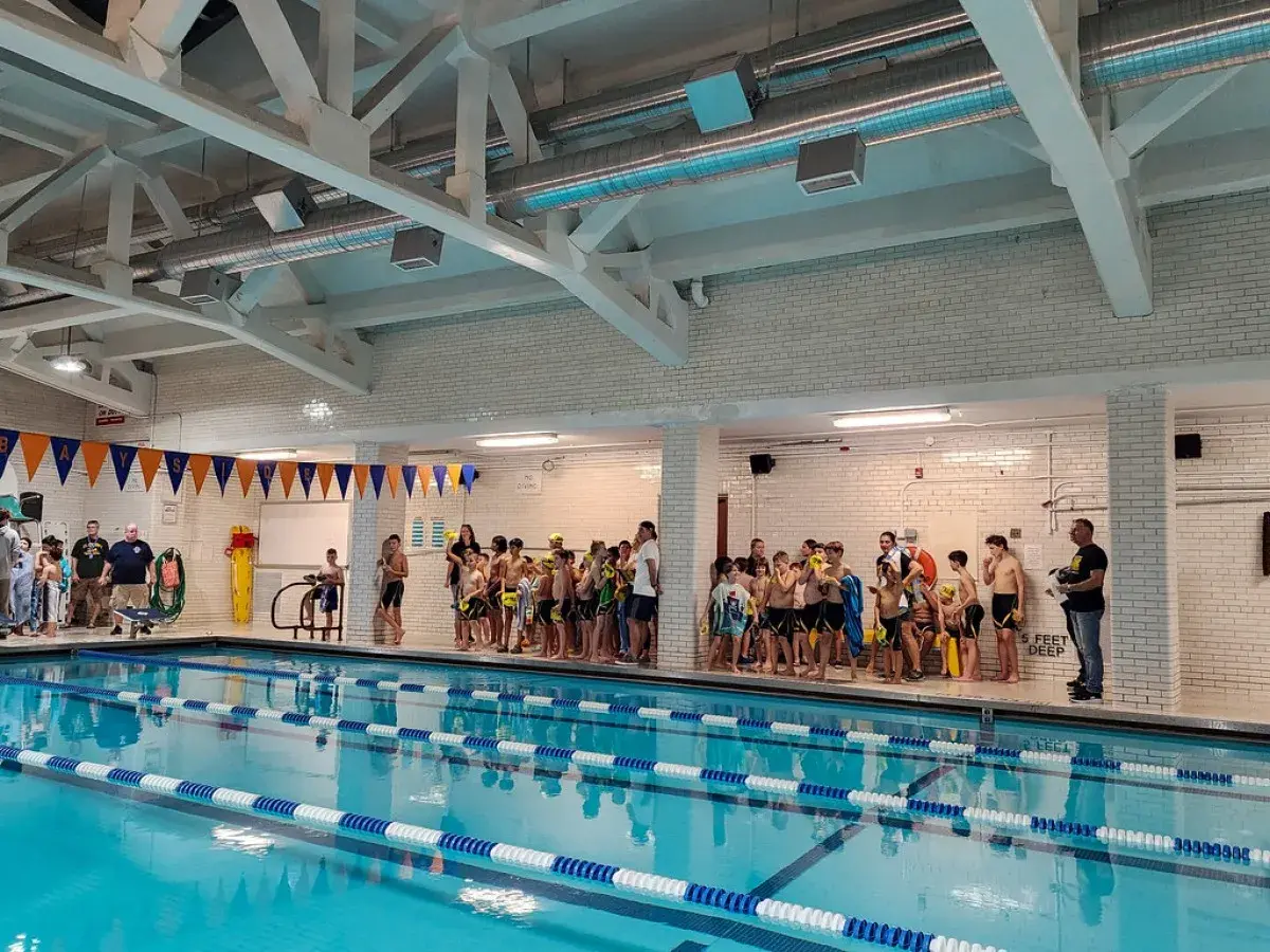 Children in swimsuits gather by the pool at Jim Montgomery Swim School, ready for lessons.