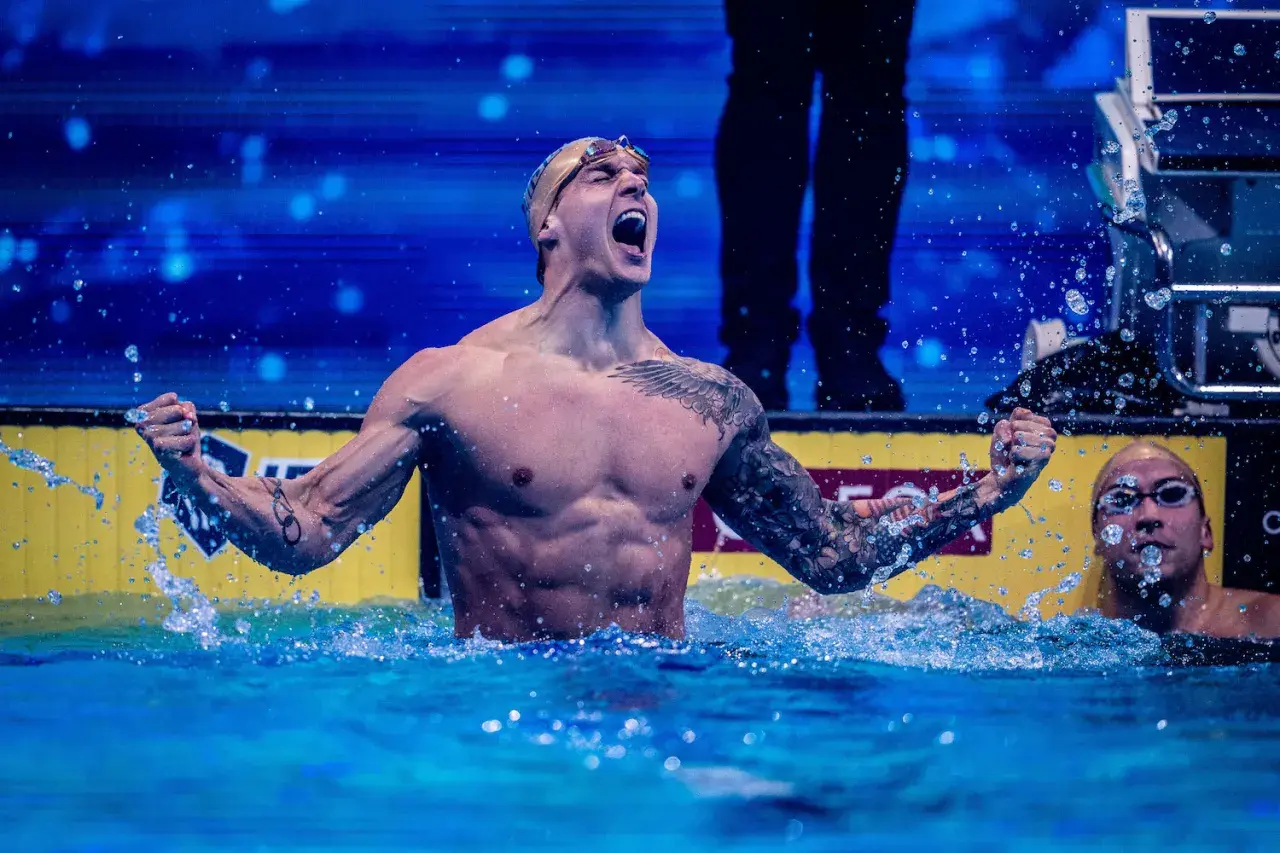 A triumphant swimmer, showcasing why swimmers have broad shoulders, celebrates in the water.