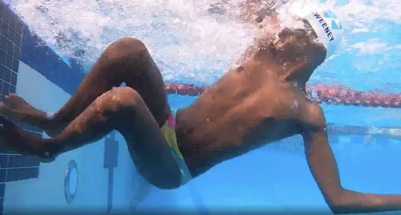Underwater view of a swimmer performing a breast stroke, with arms extended forward and legs bent, showing the technique.