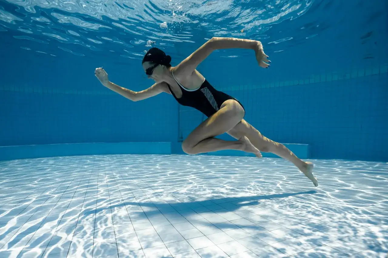 Underwater view of a woman swimming laps. She's wearing a black swimsuit and cap. This image inspires questions about how long to swim for exercise.