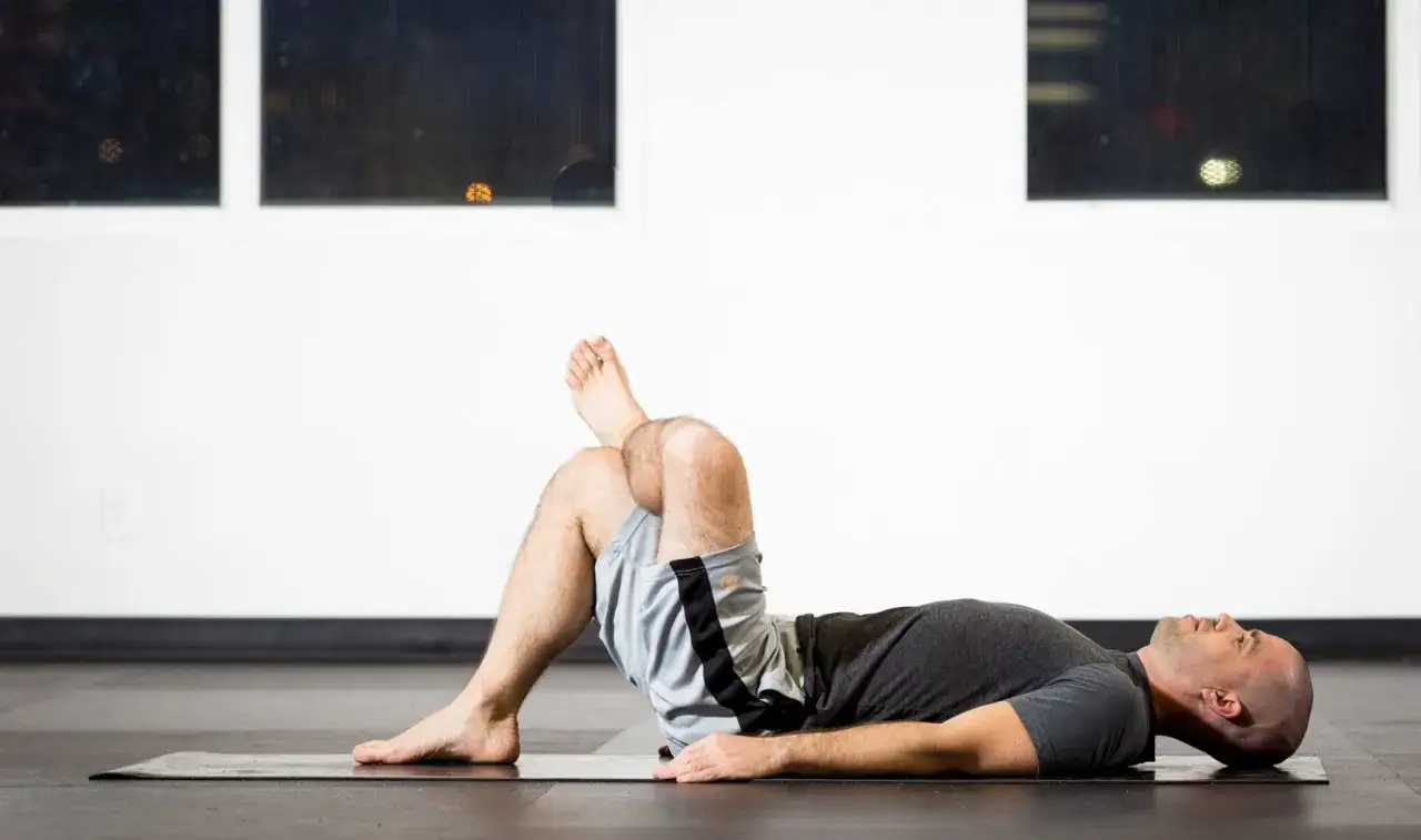 Man lying on yoga mat, one leg bent with ankle on opposite knee. Perfect yoga for swimmers to stretch hips and improve flexibility.