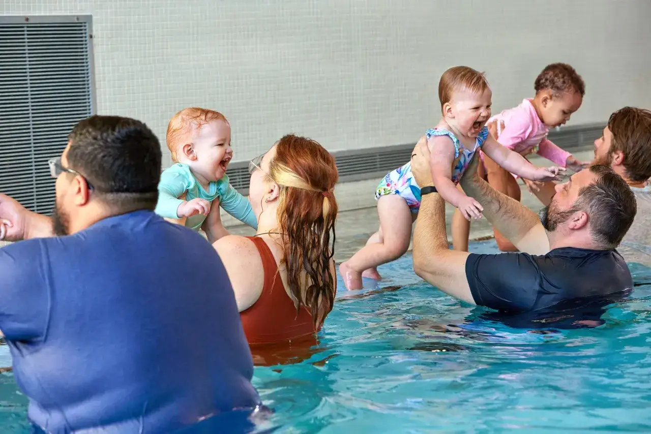 Parents and instructors joyfully interact with babies during swim tots class. Laughter fills the pool as little ones splash and play.
