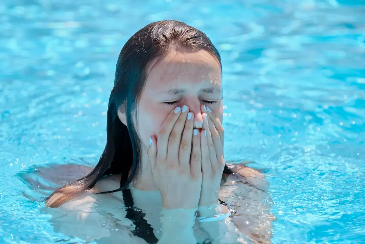 A girl in a pool covers her nose, possibly with a stuffy nose after swimming.