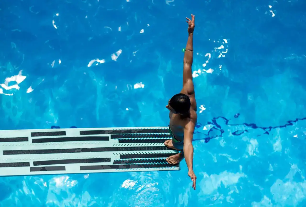 A diver poised for competitive diving, arms outstretched, ready to leap into the blue water.