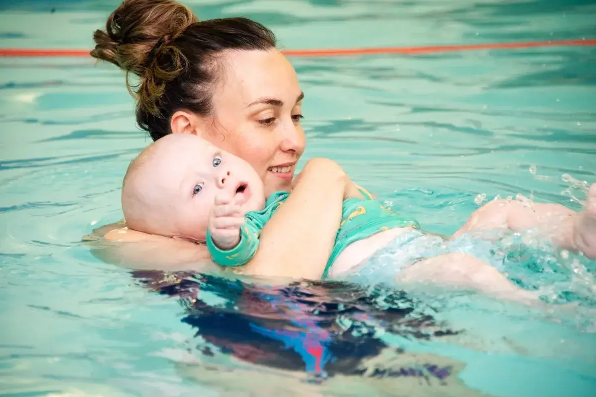 Mom and baby enjoying swim lessons for 1 year old. The baby looks surprised as water splashes.