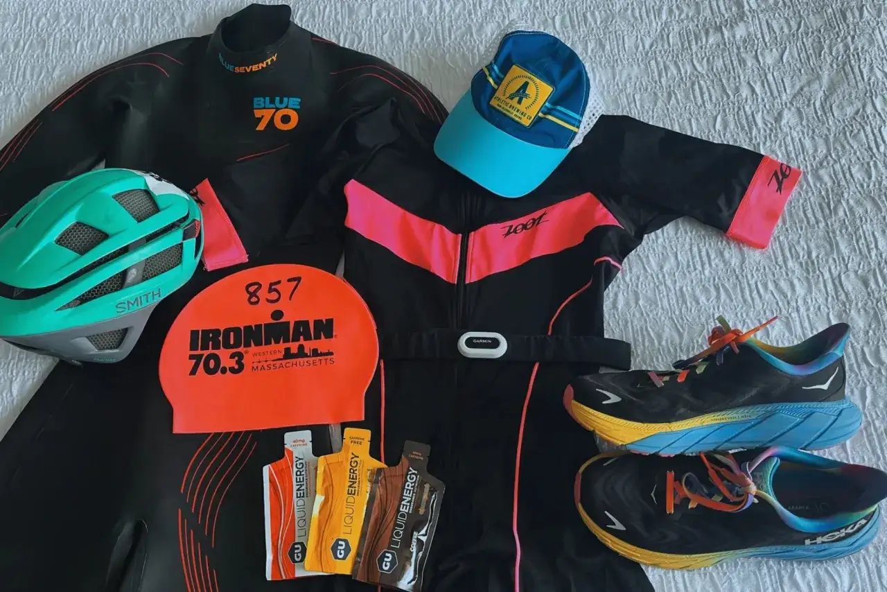 Triathlon apparel laid out: wetsuit, helmet, swim cap, cycling jersey, running shoes, and energy gels.