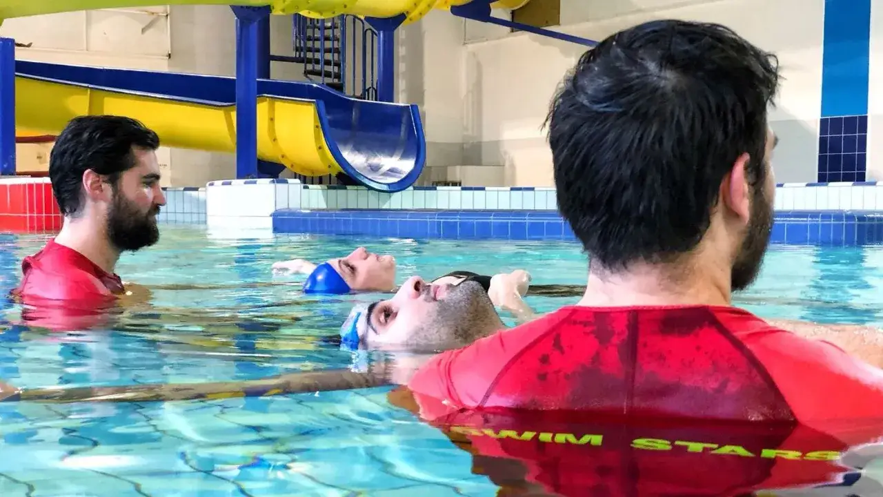 Adults with fear of water learn to float during swim lessons. A supportive instructor guides them in the pool.