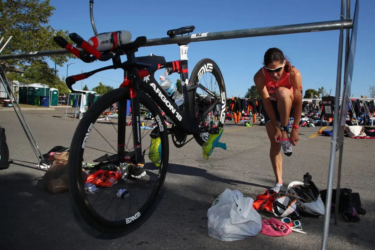 Triathlon newbies prepare for the race. A woman puts on socks next to her bike, surrounded by gear.