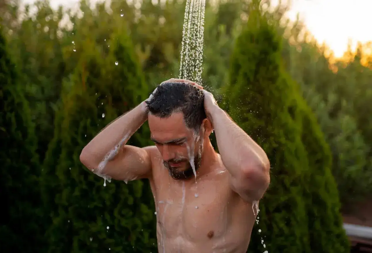 Man washing his hair outdoors, perhaps to rinse off chlorine after swimming, showing his relief from chlorine sensitivity.
