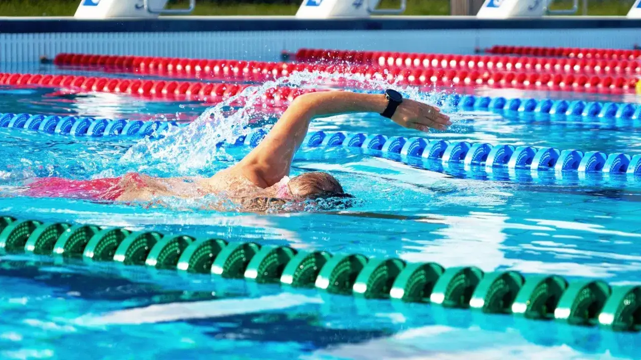 Swimmer in lane, pushing hard for VO2 max training. Water splashes as they power through the pool.
