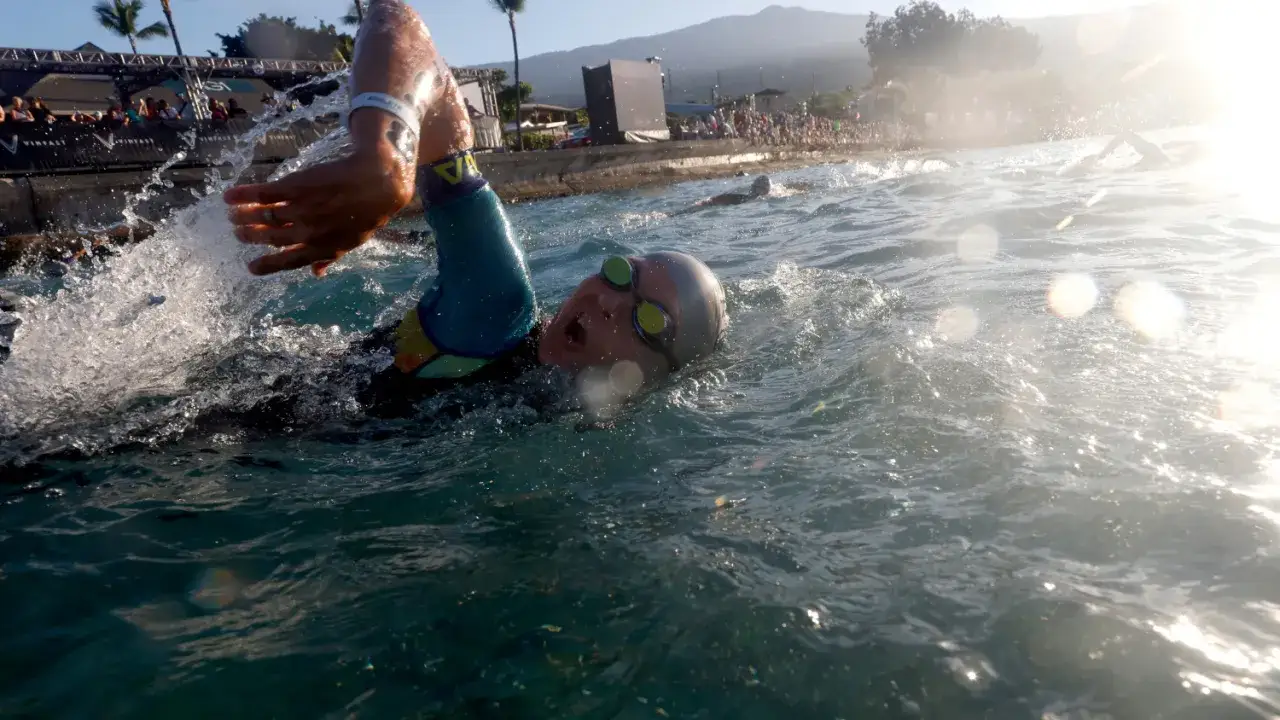 Swimmer powering through the water in Kona, Hawaii. The sun glints off the waves, a scene reminiscent of a powerful tsunami of effort.