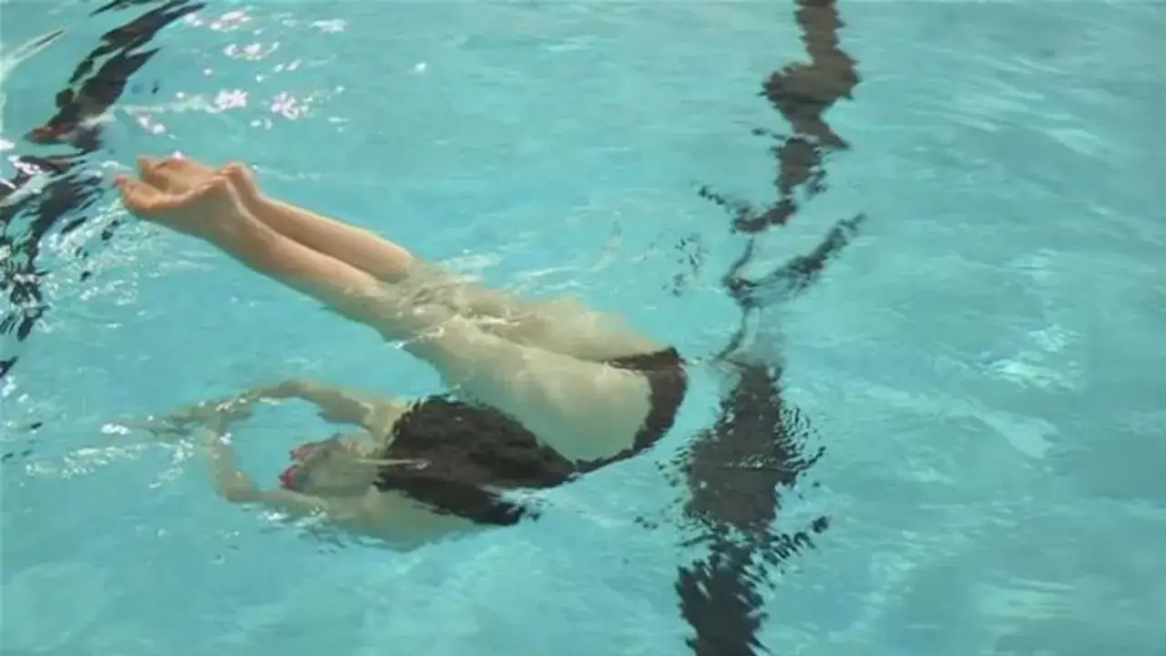 A swimmer in a black swimsuit performs a pike position in the turquoise water, legs bent at the hips.