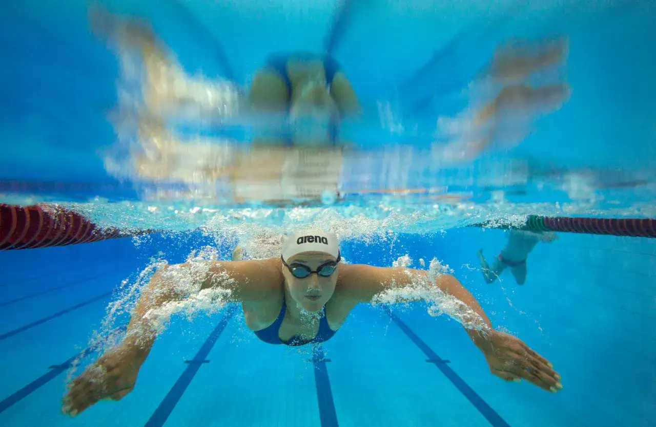 Underwater view of a female swimmer during her morning swim, focused and determined. Bubbles trail her as she glides through the clear blue water.